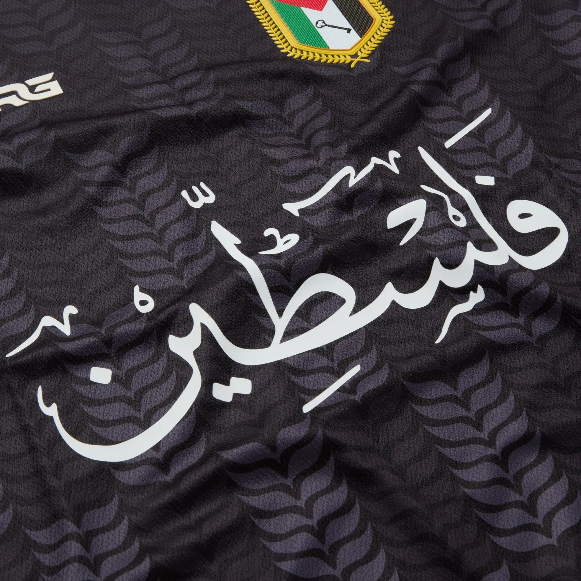 Front view of the black TRG Kids Palestine football jersey on a white background, featuring Arabic calligraphy, the Palestine badge and red and green patterned sleeves.
