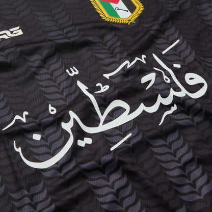 Front view of the black TRG Kids Palestine football jersey on a white background, featuring Arabic calligraphy, the Palestine badge and red and green patterned sleeves.