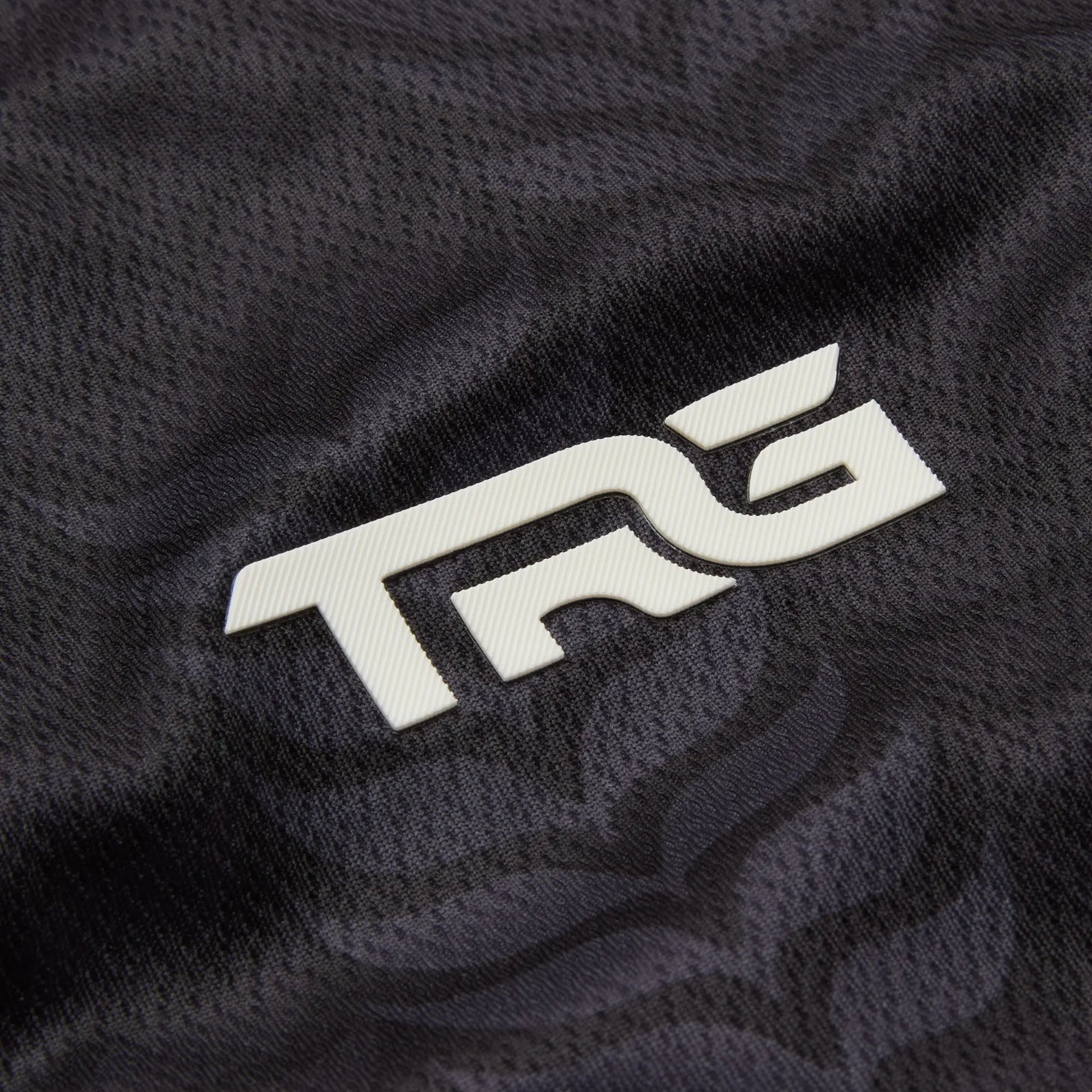 Close-up of the white TRG logo on the black Kids Palestine football jersey.