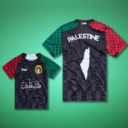 Front and back views of the black TRG Kids Palestine football jersey laid against a green background, showing Arabic calligraphy, the Palestine badge, “PALESTINE” lettering and the white map design.
