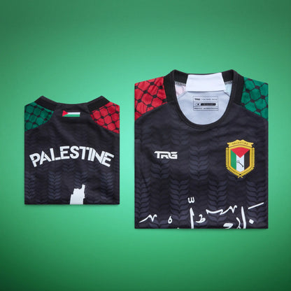 Folded front and back views of the black TRG Kids Palestine football jersey against a green background, highlighting the Arabic calligraphy, Palestine badge, “PALESTINE” lettering and neck flag detail.