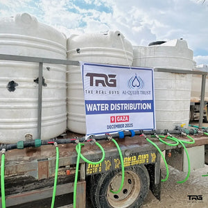 Water distribution setup with tanks and The Real Guys sign in Gaza