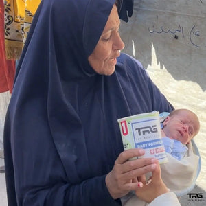Woman holding newborn baby and The Real Guys baby formula in North Gaza